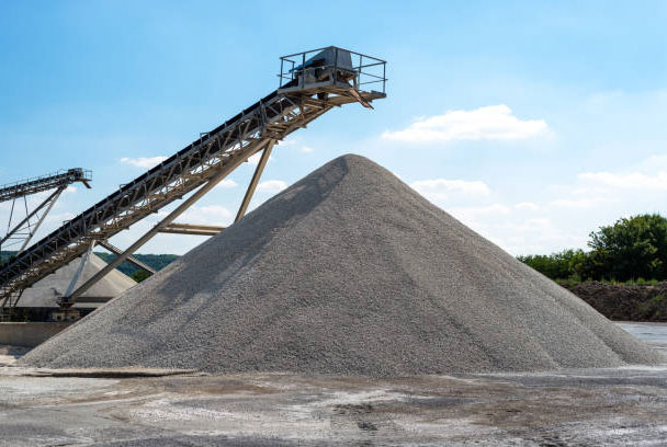 Conveyor over heaps of gravel on blue sky at an industrial cement plant.